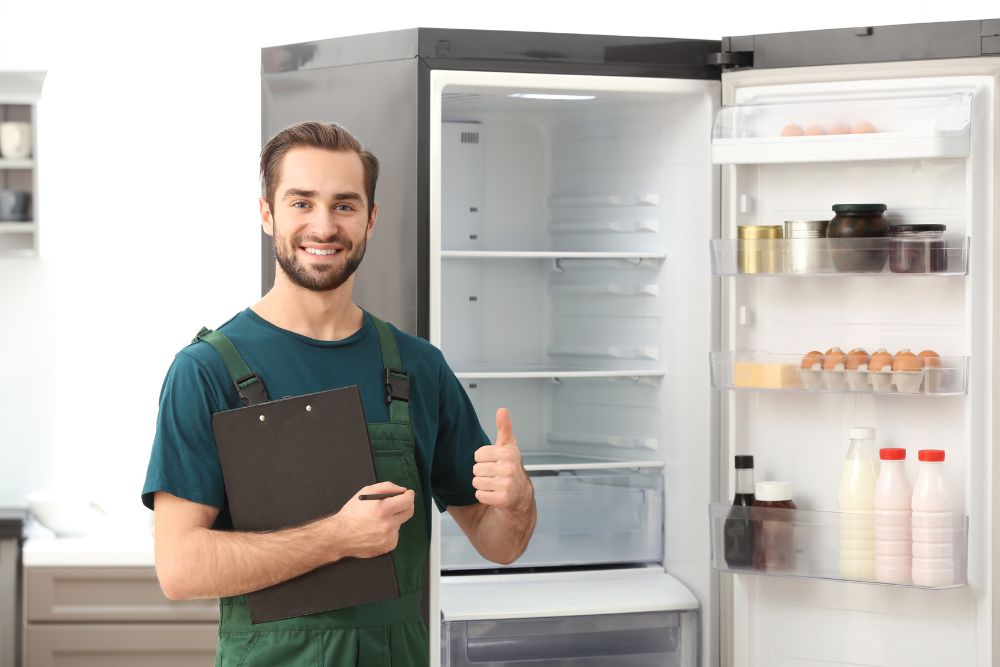 A man wearing overalls stands next to an open refrigerator, representing appliance repair services in Washington, DC.