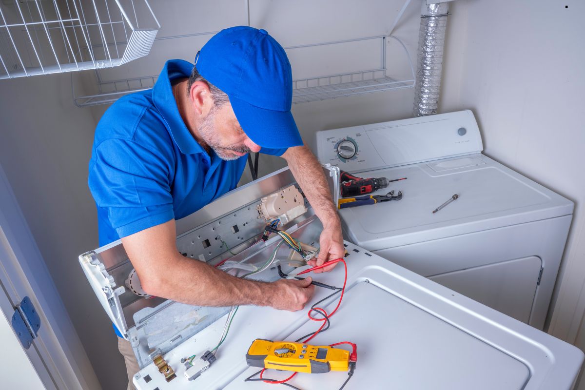 A technician repairs a washing machine, using a multimeter and tools, with wires and components visible inside the appliance.